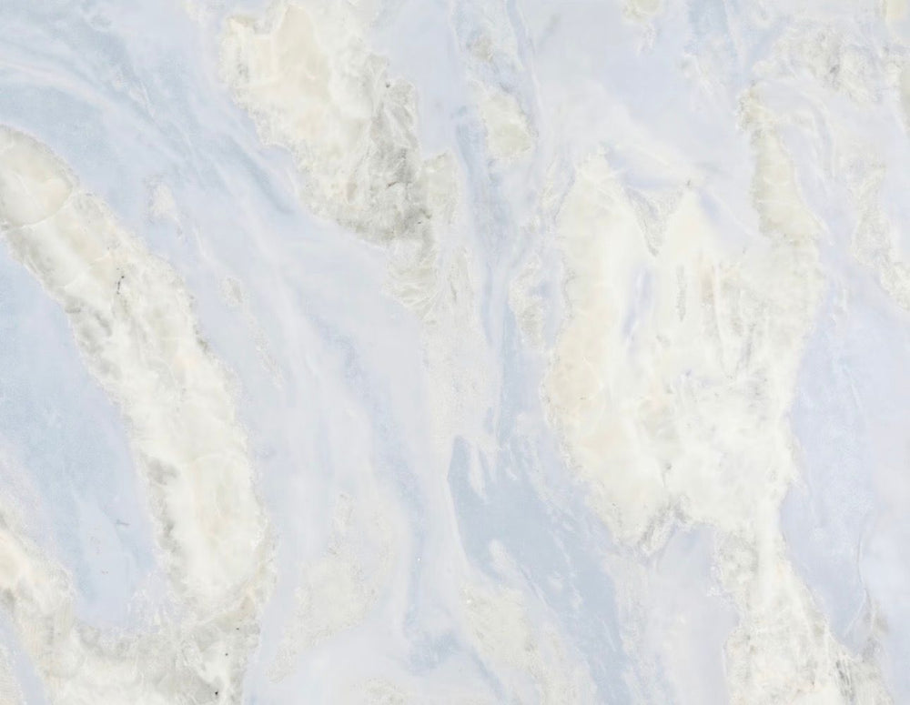 A close-up of a light marble or stone surface with soft white and pale blue veining and subtle gray marbling.