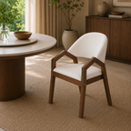 A modern wooden dining chair with a white upholstered seat and curved back, shown in a warm, sunlit room next to a round wooden table.
