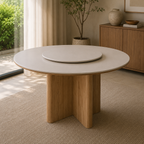 A round dining table with a light beige top and a natural wood pedestal base, featuring a matching round tray on top, set in a modern, sunlit room.