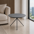 A round black side table with a thin tripod metal base, positioned in a modern living room next to a beige sofa and a large window with a city view.