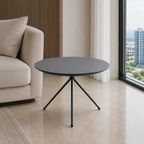A round black side table with a thin tripod metal base, positioned in a modern living room next to a beige sofa and a large window with a city view.