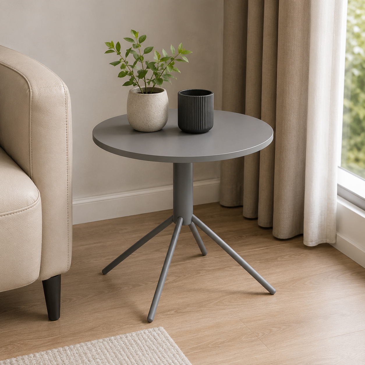 A round gray side table with a three-legged metal tripod base, styled in a living room next to a beige armchair with a potted plant and a dark gray cup on top.