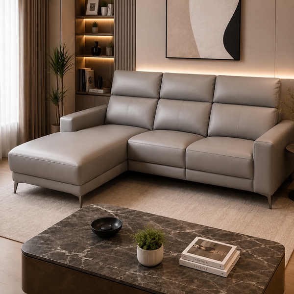 A modern L-shaped sectional sofa upholstered in light taupe leather, styled in a contemporary living room with a marble coffee table, built-in shelving, and warm ambient lighting.