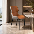 A modern dining chair with a warm brown leather seat and backrest, light gray fabric side panels, and slim black metal legs, positioned next to a marble-topped table in a contemporary dining room setting.