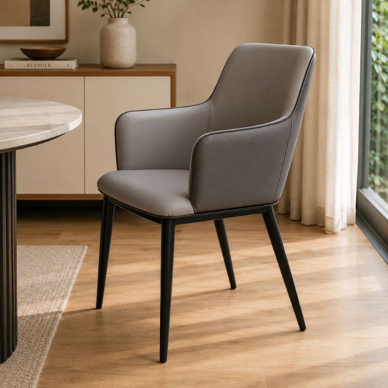 A modern gray upholstered dining chair with black tapered legs, shown in a bright, contemporary room with light wood floors, a window, and neutral decor.