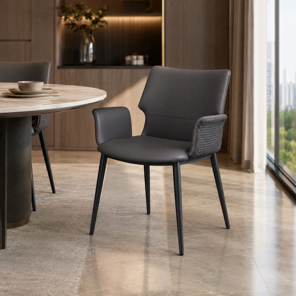 A modern dark gray upholstered dining chair with woven armrests and slim black legs, shown in a contemporary dining room setting next to a round table.