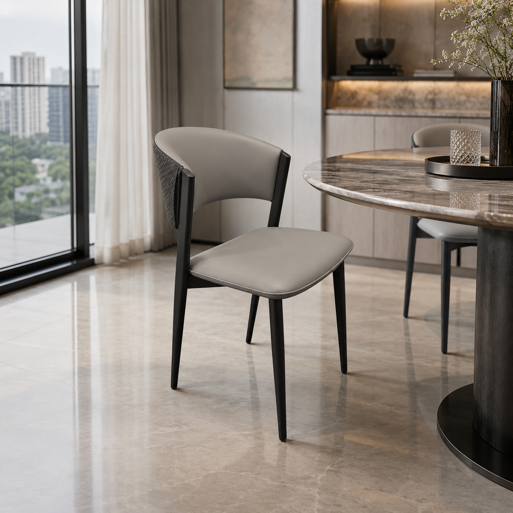 A modern dining chair with a light gray upholstered seat and curved backrest, supported by black tapered legs, shown in a contemporary dining room next to a marble-top table.