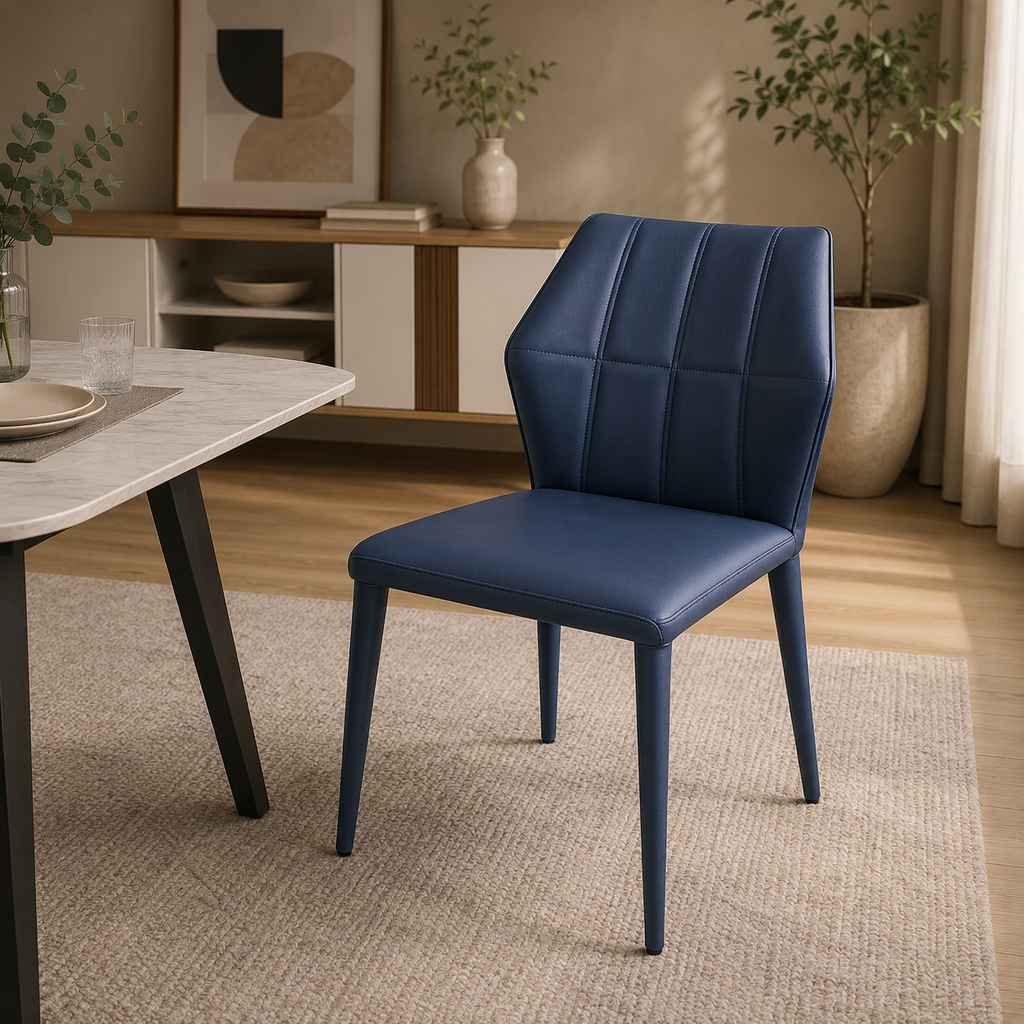 A modern dining chair upholstered in dark blue faux leather with a quilted backrest and tapered legs, shown in a styled dining room setting next to a marble table.