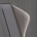 Close-up of a gray leather chair with gold stitching on a wooden floor.