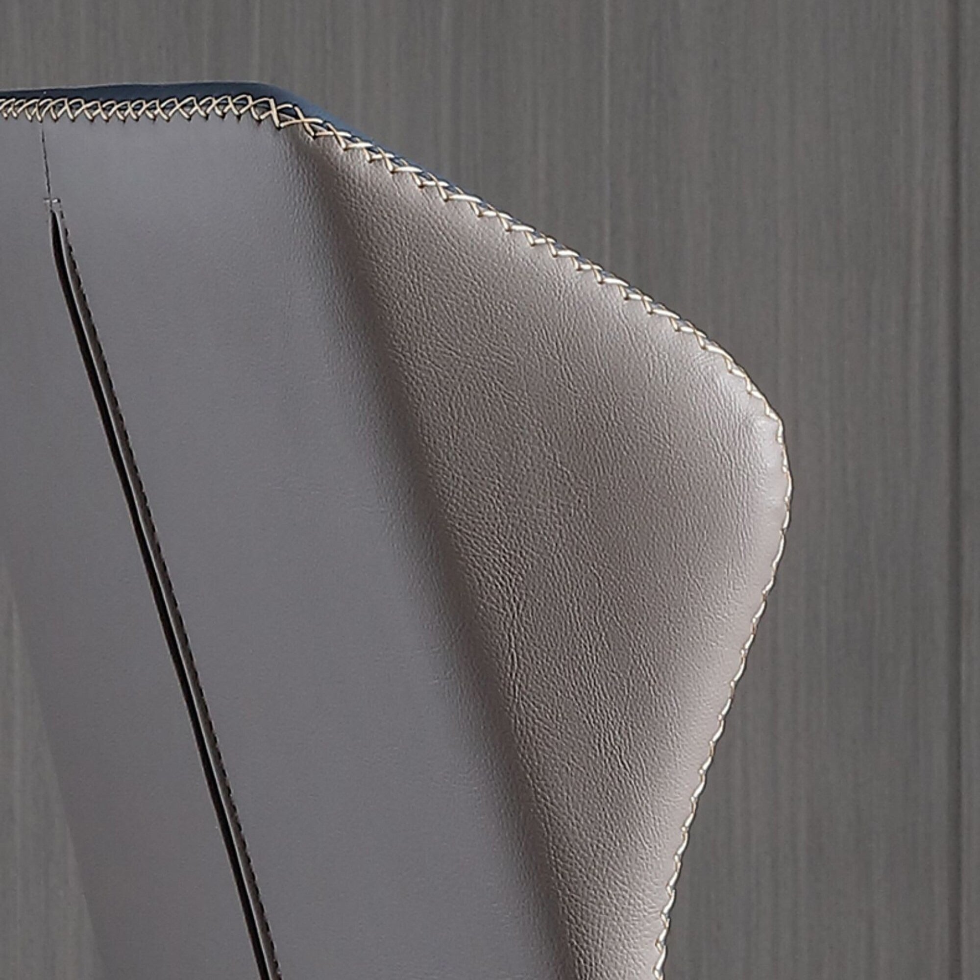 Close-up of a gray leather chair with gold stitching on a wooden floor.