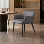 A modern gray upholstered dining chair with tapered black legs, shown in a contemporary dining room setting with a marble-topped table and warm wood cabinetry in the background.