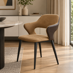 A modern dining chair with a curved tan upholstered seat and back, dark brown side panels, and tapered black metal legs, shown in a styled dining room setting.