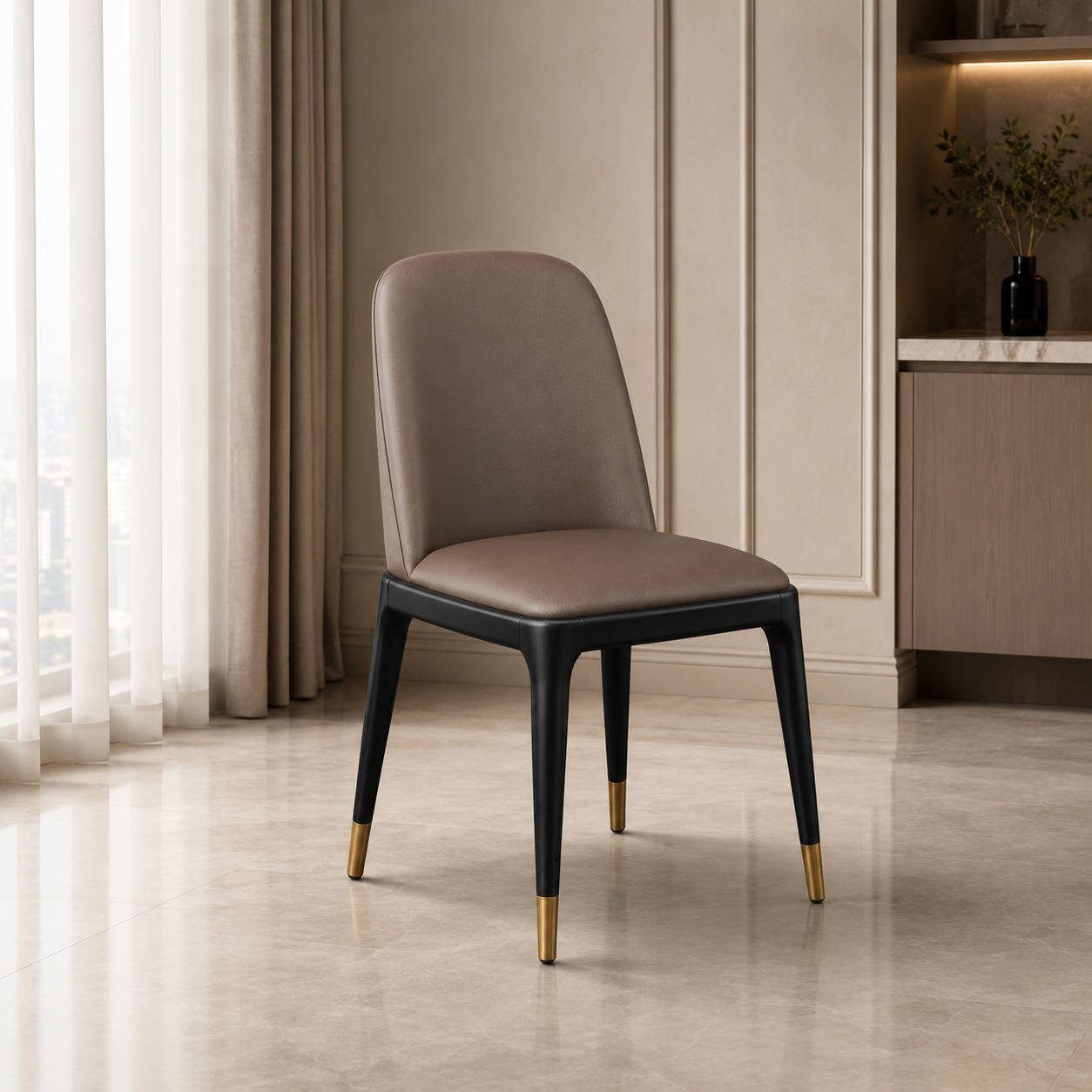 A modern dining chair with a taupe-brown upholstered seat and curved backrest, supported by black tapered legs with gold-tone metal caps, set in a contemporary interior room.