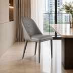 A modern gray upholstered dining chair with a curved, ribbed backrest and tapered legs, positioned in a contemporary kitchen or dining area next to a marble-topped table.