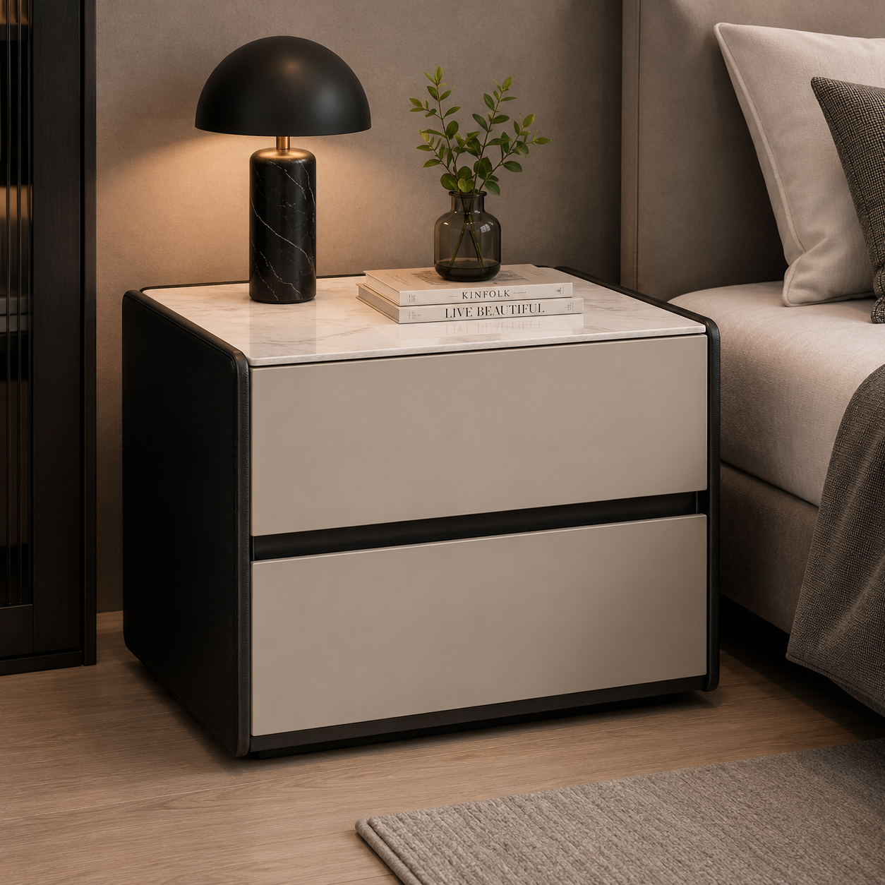 A modern two-drawer nightstand with a cream-colored front and black frame, styled in a bedroom next to a bed with a black table lamp and a small plant on top.
