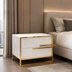 A modern two-drawer nightstand with a glossy white finish and polished gold metal frame, positioned next to a bed in a contemporary bedroom setting.