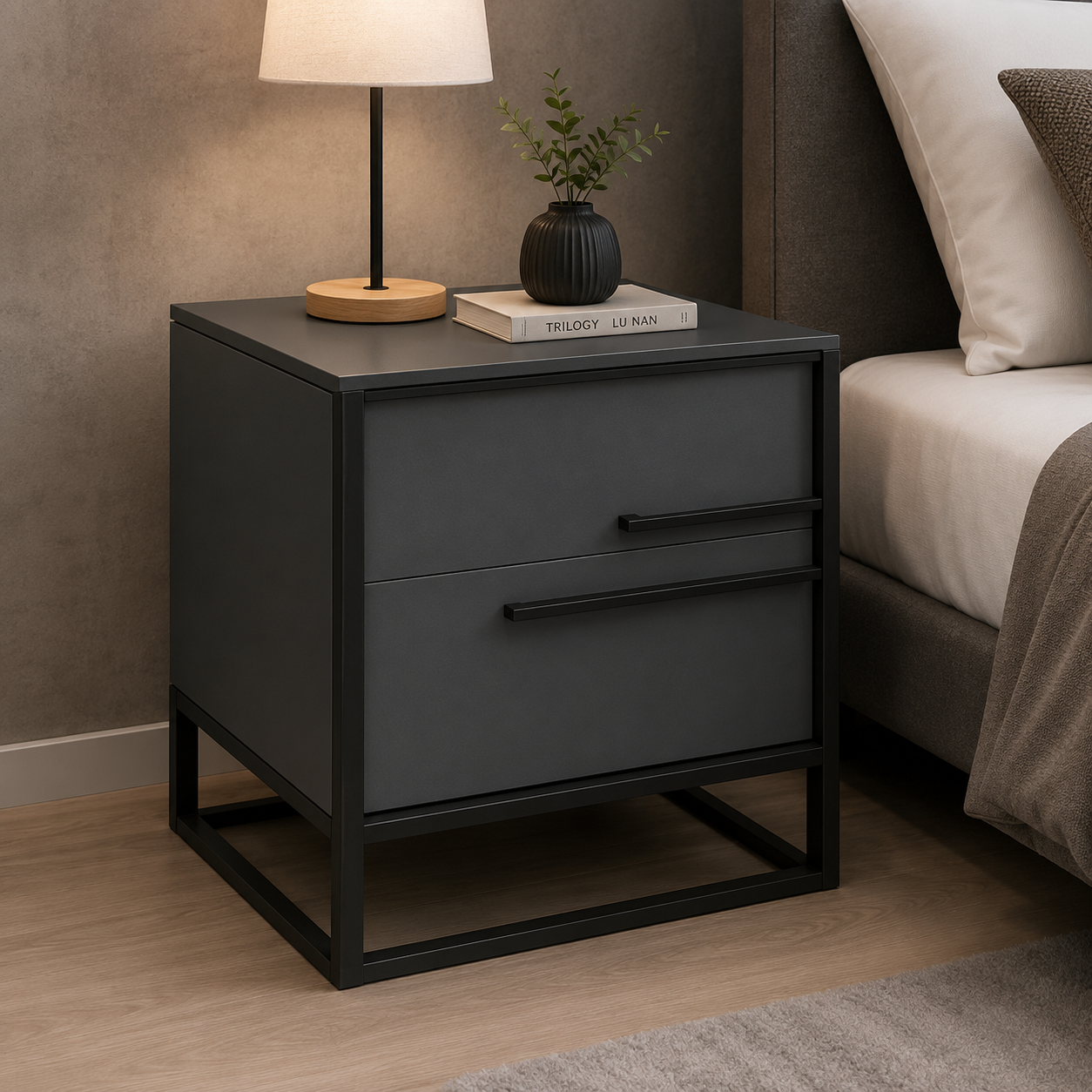 A modern two-drawer nightstand in matte dark gray with a black metal frame and handles, styled in a bedroom next to a bed with a lamp and a small plant on top.