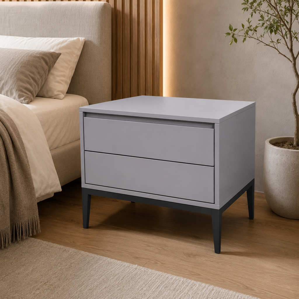 A modern two-drawer nightstand in light gray with dark gray legs, positioned next to a bed in a styled bedroom setting.