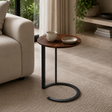 Small round wooden side table with a black metal base in a living room setting.