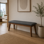 Wooden bench with a gray cushion in a living room setting with a plant and framed art on the wall.