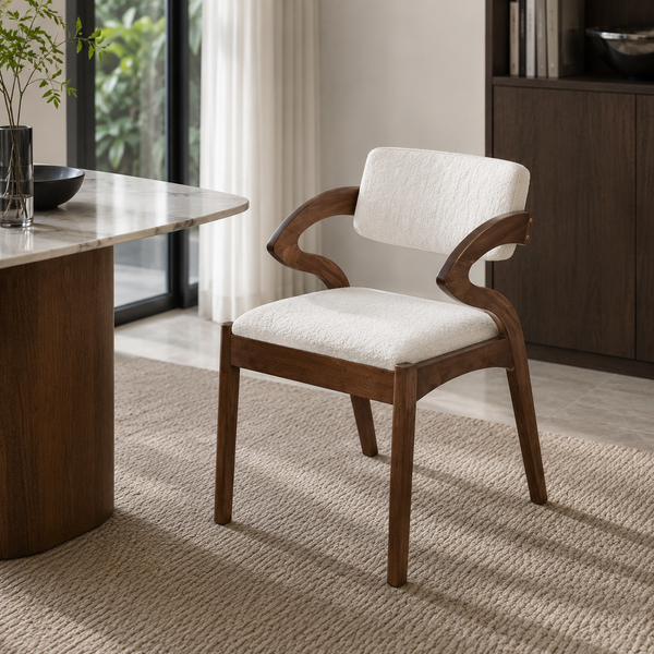 A modern wooden dining chair with curved armrests and white textured upholstery, placed in a bright, contemporary room next to a marble-topped table.