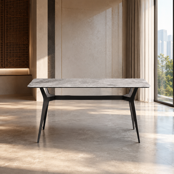 A modern rectangular dining table with a gray stone-look top and black metal legs, set in a minimalist, sunlit interior with beige walls and floor.