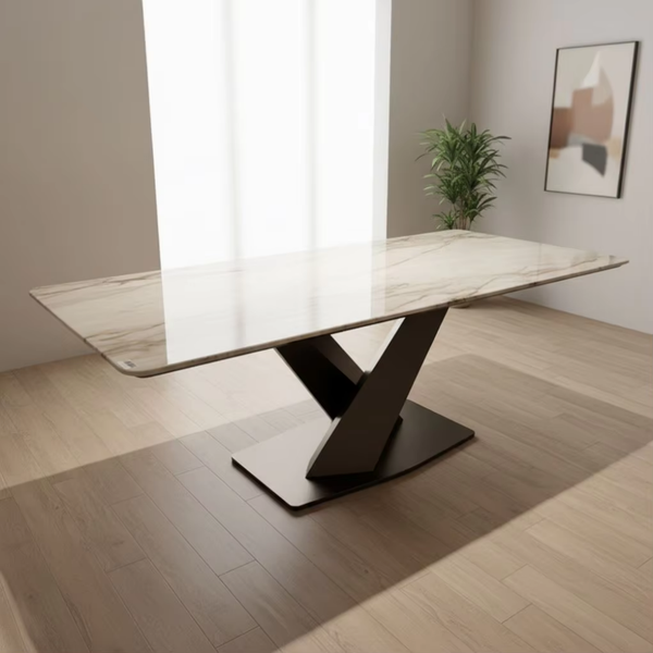 Modern dining table with marble-like surface and black metal base in a room with light wood flooring and a plant.