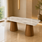A modern rectangular dining table with a white marble-patterned top and two tapered wooden legs, shown in a warm, contemporary interior setting.
