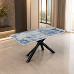 A rectangular dining table with a blue and white marbled stone-look top and black crossed metal legs, shown in a modern interior room with tiled floors and large windows.