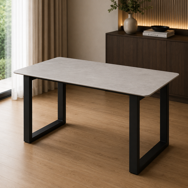 A rectangular dining table with a light gray stone-look top and black metal legs, shown in a modern room setting with wood flooring and a dark wood cabinet in the background.